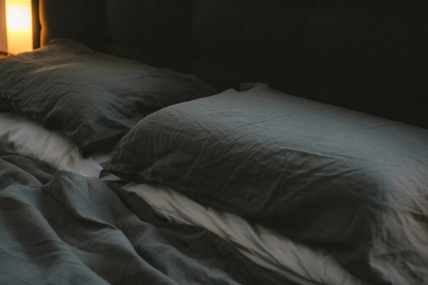Dimly lit bedroom with charcoal linen sheets and warm ambient light - lifestyle mood image